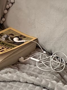 an open book laying on top of a bed next to ear buds and headphones