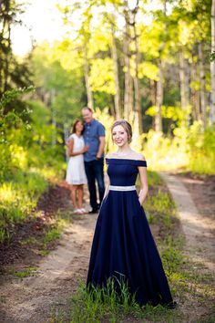 a woman in a blue dress standing on a dirt road next to a man wearing a blue shirt and tie