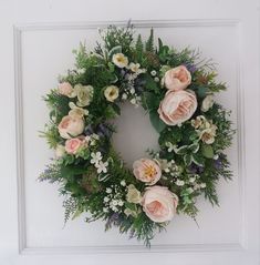 a wreath with pink flowers and greenery hanging on a white door frame in front of a wall