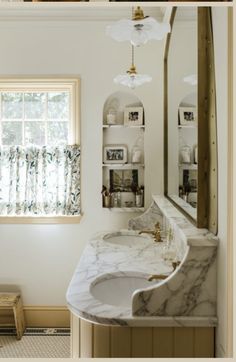 a bathroom with marble counter top and white walls, along with a gold framed mirror