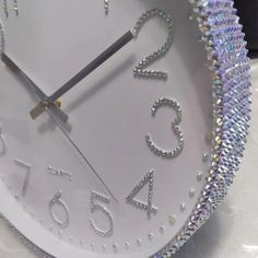 a white clock with silver numbers on it's face and some beads around the edges