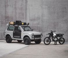 an off - road vehicle parked next to a motorbike on the sidewalk in front of a concrete wall