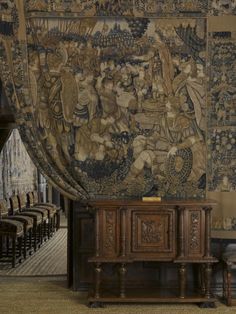 an old tapestry hanging on the wall next to a wooden table with chairs in front of it