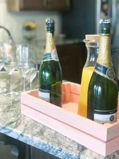 two bottles of champagne are sitting in a tray on the kitchen counter next to wine glasses