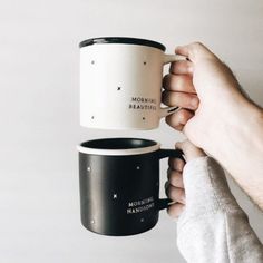 someone holding two coffee mugs in their hands, one is black and the other is white