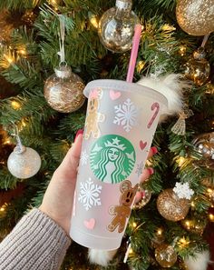 someone holding up a starbucks cup in front of a christmas tree with ornaments on it