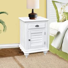 a white nightstand with a lamp on it next to a bed and a green pillow