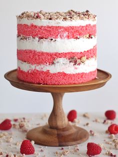 a red, white and blue cake with raspberries scattered around it on a wooden stand