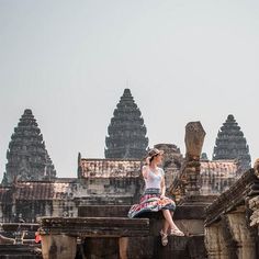 a woman sitting on top of a stone wall next to an old building with many spires