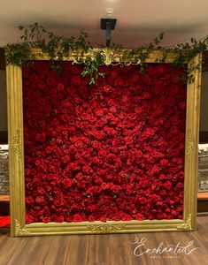 a large gold frame with red flowers on the wall and greenery hanging over it