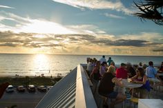 a group of people sitting on top of a balcony next to the ocean at sunset