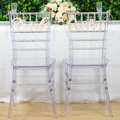 two clear chairs sitting next to each other in front of a table with flowers on it