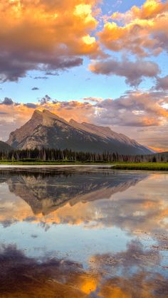 the mountains are reflected in the still water at sunset with clouds and trees around them