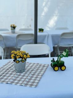 a table topped with a vase filled with yellow flowers next to a green toy tractor