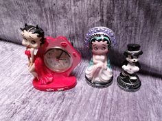 three small figurines sitting next to each other near a clock on a table