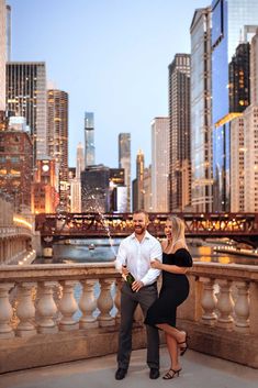 a man and woman standing on top of a bridge in front of the city skyline