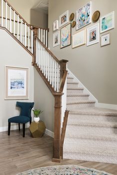 a staircase with pictures on the wall and a blue chair next to it in a living room