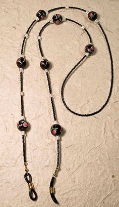 This eyeglass leash features black glass lamp work beads with tiny roses, black Japanese seed beads and white glass Japanese cube beads for accent.  The ends are black rubber with either gold or silver tone spirals.  Average length is about 27-28 inches, but can be longer or shorter, if requested. Black Glass Beaded Jewelry, Handmade Black Glass Beads, Handmade Glass Beads In Black, Black Glass Beaded Necklaces With Beaded Chain, Black Glass Beaded Necklace With Beaded Chain, Adjustable Glass Beaded Necklace With Black Beads, Adjustable Black Beaded Glass Necklaces, Adjustable Black Beaded Glass Necklace, Black Glass Round Bead Jewelry