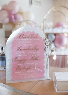 a pink and white wedding stationery on a wooden table with balloons in the background