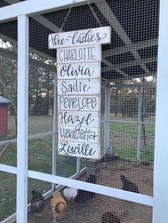 a sign hanging from the side of a white fence in front of a pig pen