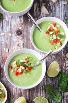 two white bowls filled with green soup and garnished with chopped vegetables, sliced limes and peanuts