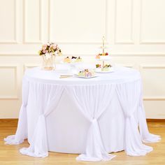 a white table topped with two cakes covered in frosting and sitting on top of a hard wood floor