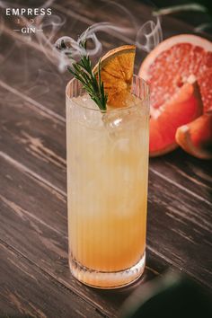 a drink with an orange slice and rosemary garnish on the rim next to grapefruit