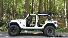 a white jeep parked on the side of a road in front of some tall trees