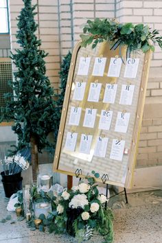 a wedding seating chart with flowers and greenery on the floor next to it is an easel