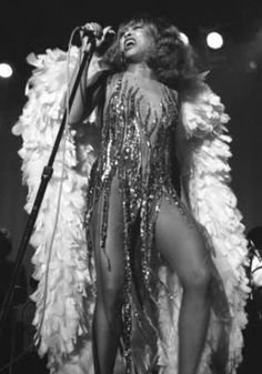 a woman in a feathered outfit on stage with a microphone and lights behind her