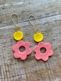 two pink and yellow flower shaped earrings on wooden surface with gold earwires hanging from them