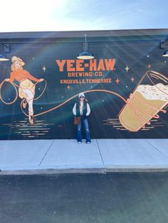 a woman standing in front of a wall with an advertisement for yeeh - haw brewing