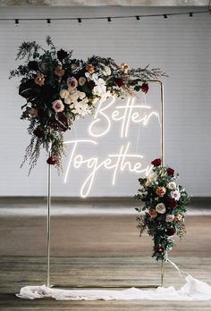 a neon sign that says better together with flowers and greenery on it in front of a white backdrop