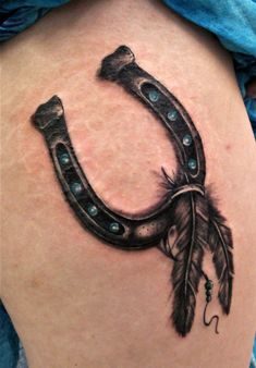 a tattoo on the back of a woman's thigh with a horseshoe and feathers