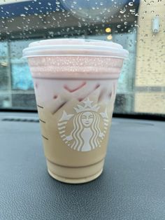 a starbucks cup sitting on top of a car dashboard next to a window covered in raindrops