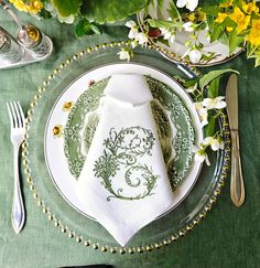 a place setting with green and white linens, silverware, and yellow flowers