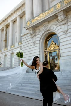 a bride and groom walking down the street in front of an old building with columns