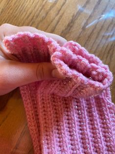 a child's hand holding a pink knitted mitt on top of a wooden table