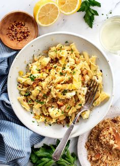 a white bowl filled with pasta and garnished with parsley next to lemon slices