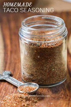 a glass jar filled with spices on top of a wooden table next to a spoon