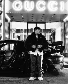 a man standing next to a parked car in front of a gucci club sign