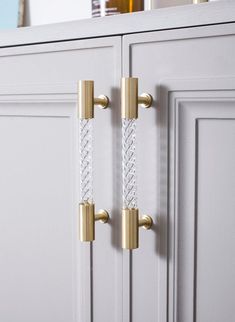 two brass handles on white cabinets with gold hardware and glass door knobs in the background