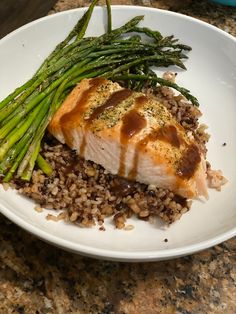 a white plate topped with meat and rice covered in sauce next to asparagus