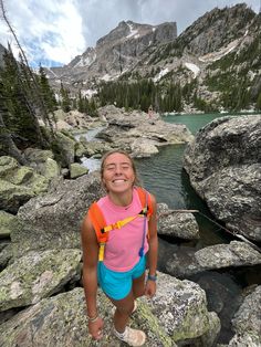 a woman standing on top of a rocky hillside next to a lake