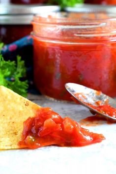 a tortilla chip being dipped with pepper and onion relish next to a jar of ketchup