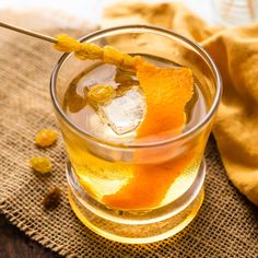 a glass filled with liquid and orange peels on top of a cloth covered table