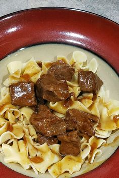 a red bowl filled with beef and noodles