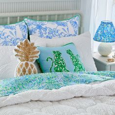 a white bed with blue and green pillows on top of it next to a lamp