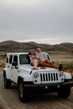 two people sitting on top of a white jeep