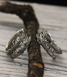 two silver rings sitting on top of a piece of driftwood next to a twig